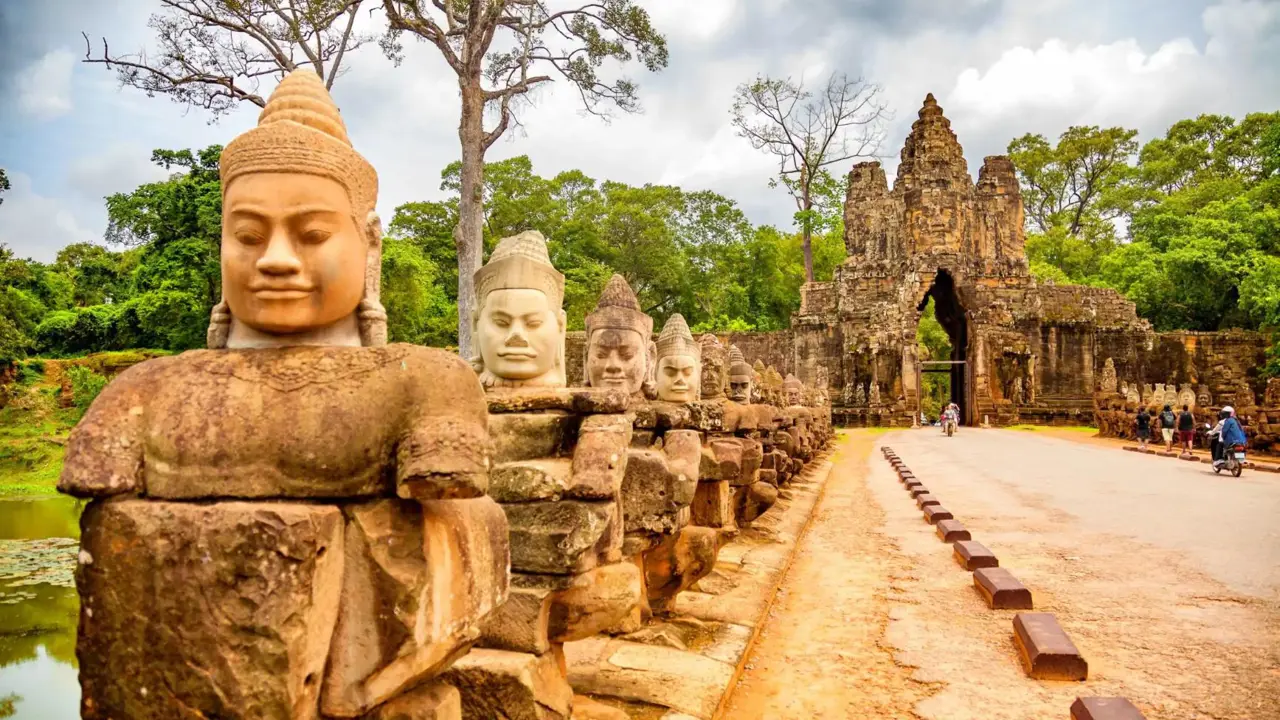 Stone statues line the entrance road to the majestic Angkor Thom gate, surrounded by dense green jungle