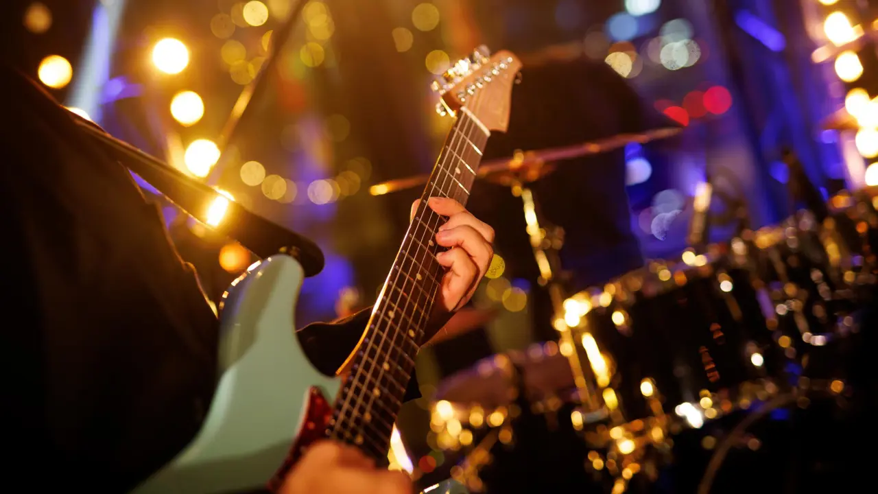 A close up of a guitarist with a drum kit in the background