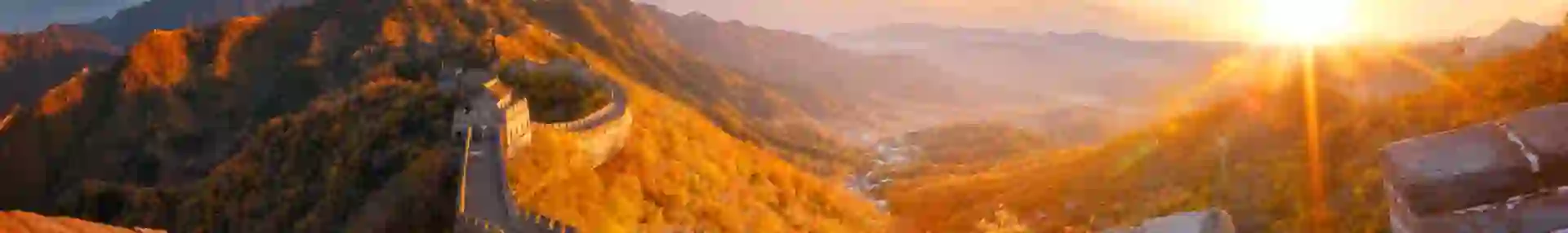 The Great Wall winding over mountain ridges, glowing in golden light at sunset, near Beijing, China