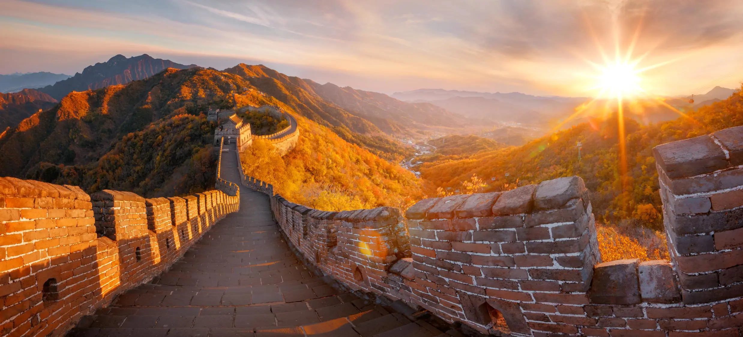 The Great Wall winding over mountain ridges, glowing in golden light at sunset, near Beijing, China