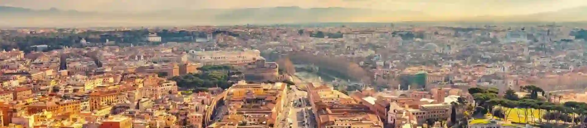 Aerial view of St. Peter’s Square in Vatican City, bathed in golden sunlight with Rome in the distance under a partly cloudy sky