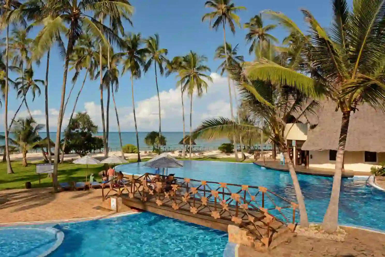The pool area at Ocean Paradise Resort & Spa in Zanzibar, featuring a large, lagoon-style swimming pool surrounded by palm trees, sun loungers and thatched-roof buildings