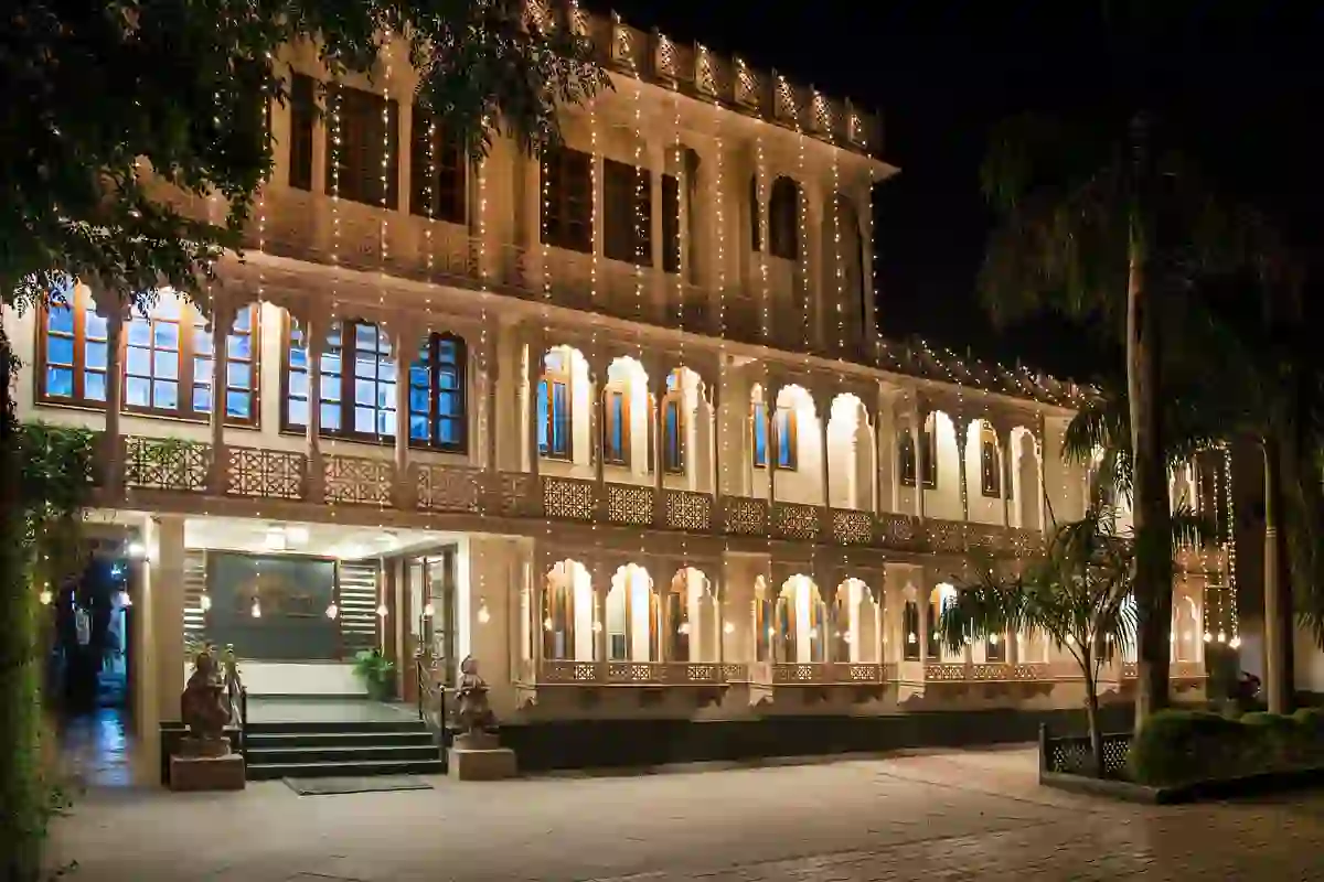 Grand exterior of the Ranthambore Bagh Palace hotel at night, with it's intricately designed façade beautifully lit by warm string lights