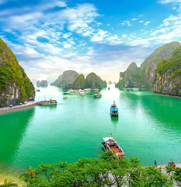 Panoramic view of Ha Long Bay in Vietnam, with emerald green waters dotted with traditional wooden boats, surrounded by towering limestone karsts and lush, forested islets under a partly cloudy sky