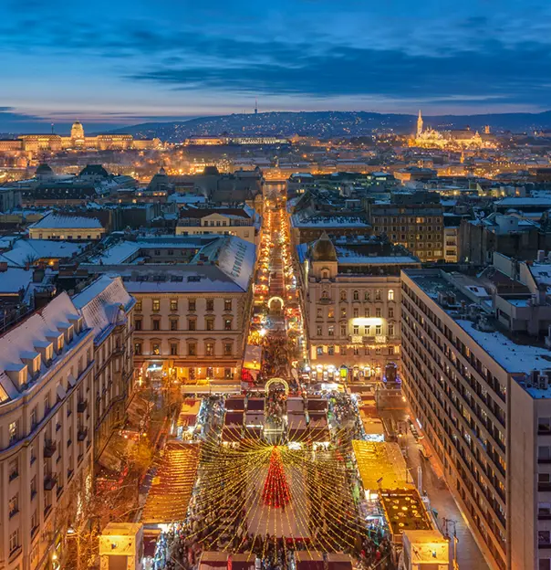 High angle shot of long street, full of people and stalls. Leading down to the forefront of the image, to the busy square with a red Christmas tree in the centre, with gold lights trailing out of it.