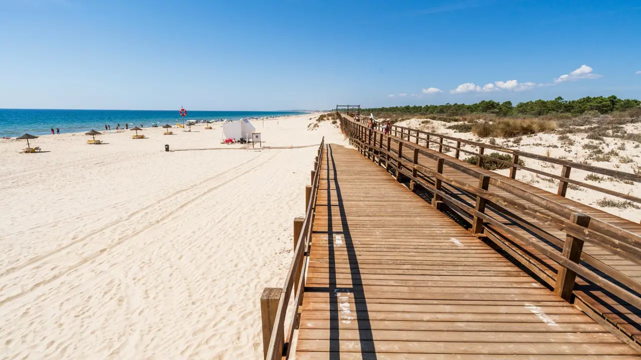 Wooden walkway on the beach at Monte Gordo on the Algarve, with the sandy beach and sea to the left and a shrub area to the right