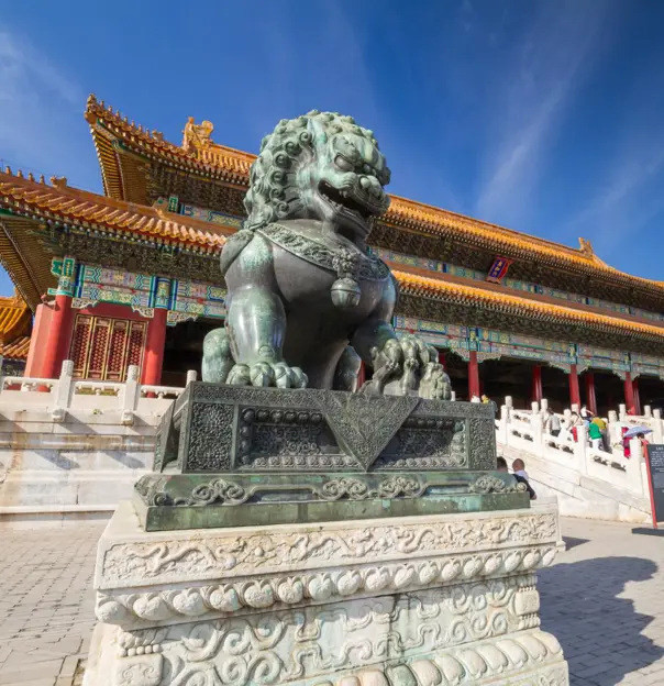 Bronze guardian lion outside ornate palace buildings in the Forbidden City, Beijing, China