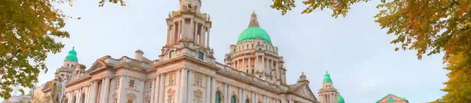Belfast City Hall, a grand Baroque Revival building with a large central dome and ornate stone façade, on an autumn day surrounded by trees with colourful yellow leaves