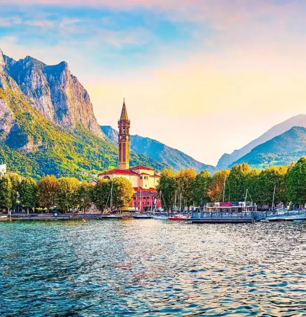A view of Lake Como with a small church tower and mountains and trees in the background