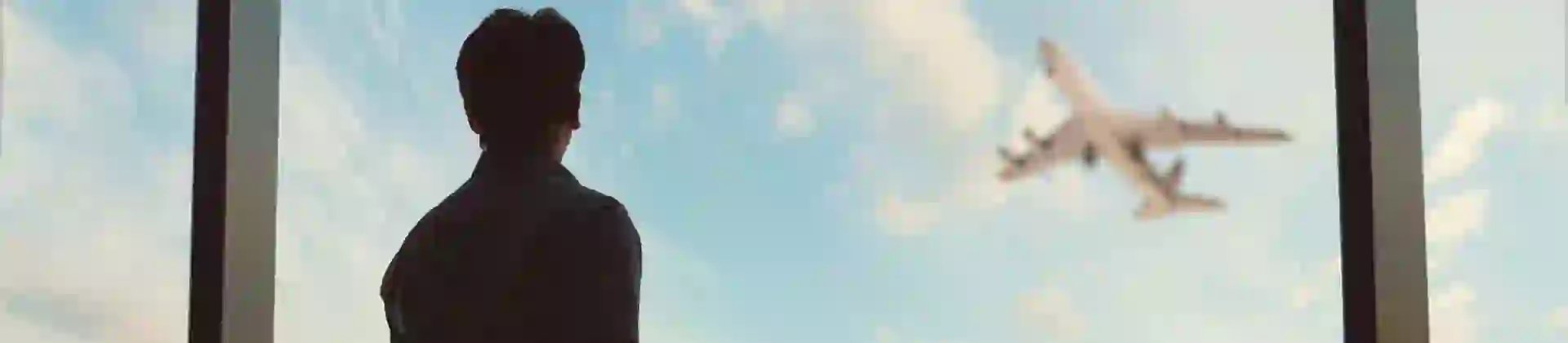 Person looking out the window in an airport at a plane taking off