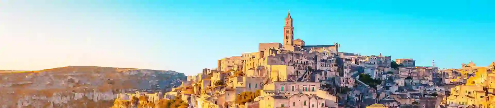 A panoramic view of the historic stone town of Matera, Italy, with ancient buildings stacked on a hillside in the golden glow of sunset
