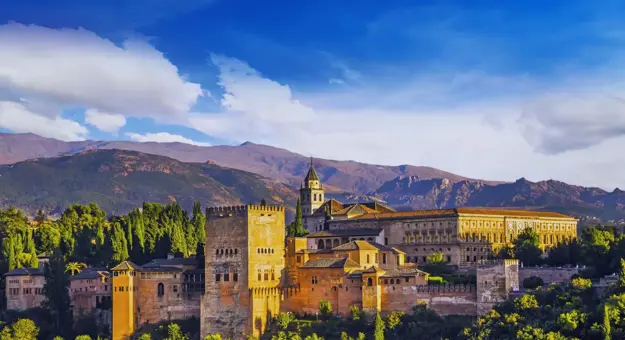 Panoramic view of the Alhambra Palace in Spain on a sunny day, with its historic architecture set against a backdrop of rolling hills and a bright blue sky