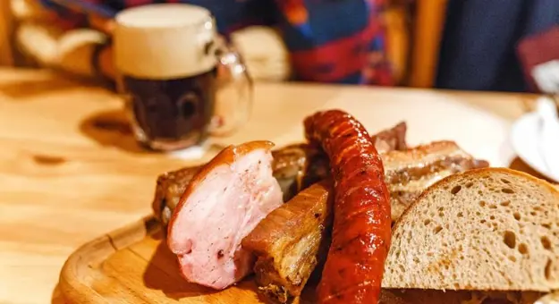 Close up of a plate of traditional sausage, pork meat and slices of bread. Crafted Czech mug of beer in the background.