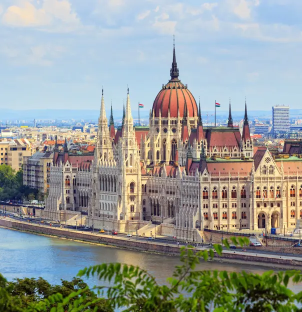 High angle shot of Hungarian Parliament Building, with red roofs and spiky turrets. Danube river in the left forefront