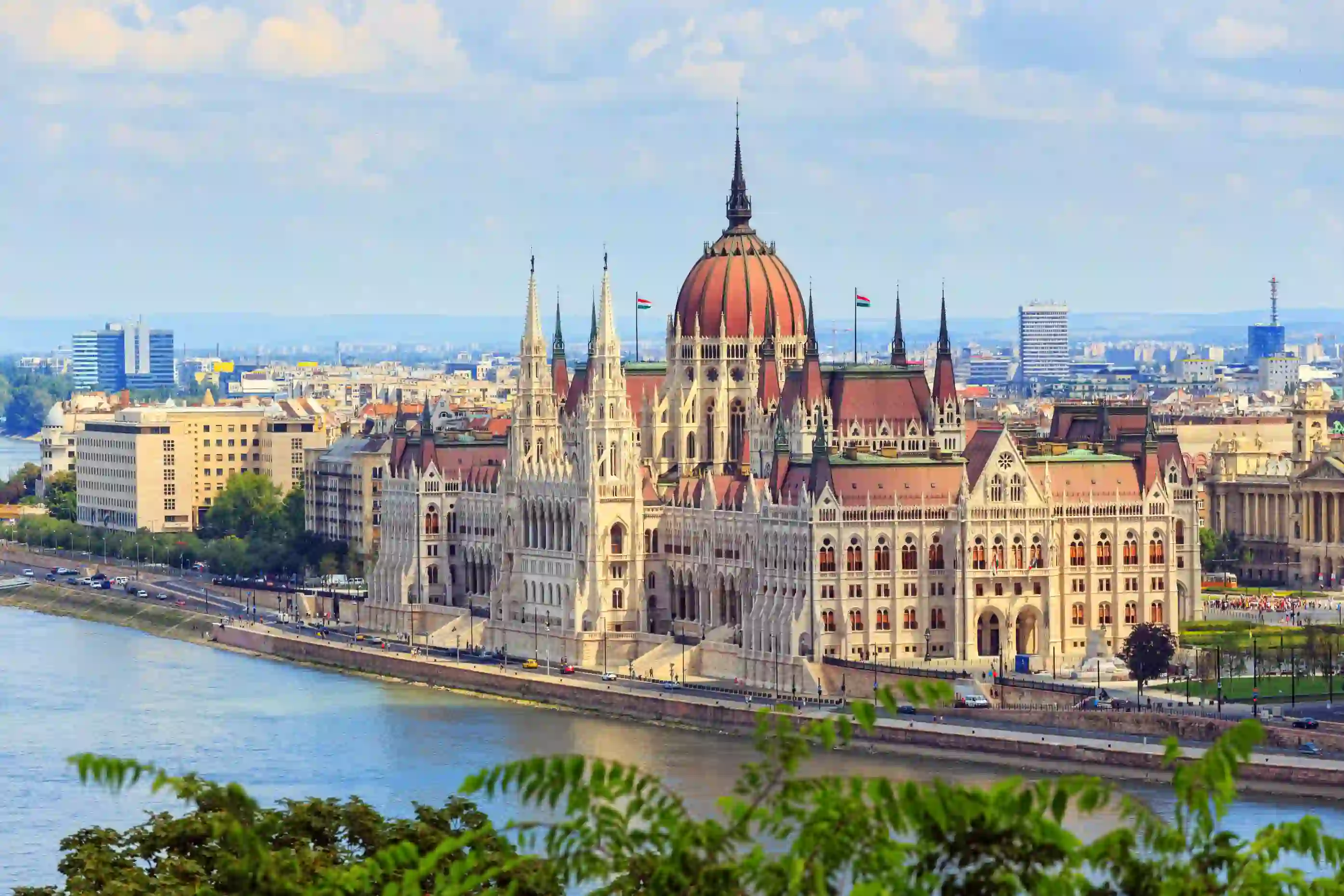 High angle shot of Hungarian Parliament Building, with red roofs and spiky turrets. Danube river in the left forefront