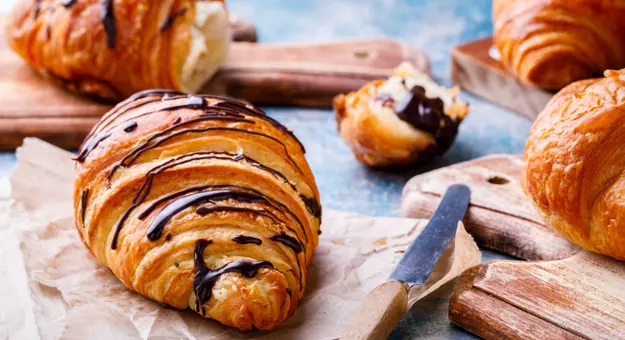 Chocolate croissants, one in the background which has been broken apart.