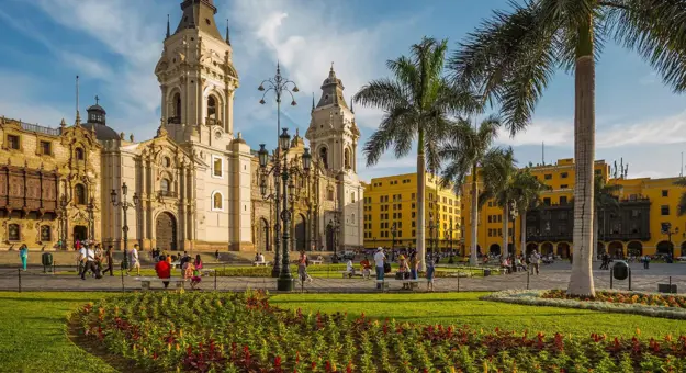 A view of the Cathedral of Lima in the Main Square of Lima, Peru, featuring colonial architecture, palm trees, and a sunny sky in the background