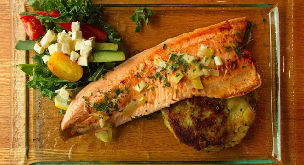 Board with dinner consisting of fish, a side salad and potato