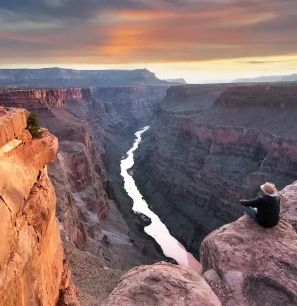 Toroweap Point at the Grand Canyon, with a person sitting near the edge, overlooking the vast canyon landscape as the sun sets