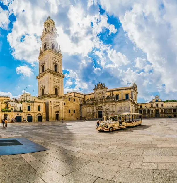 Square in Lecce, Italy, showing a tower and touring vehicle 