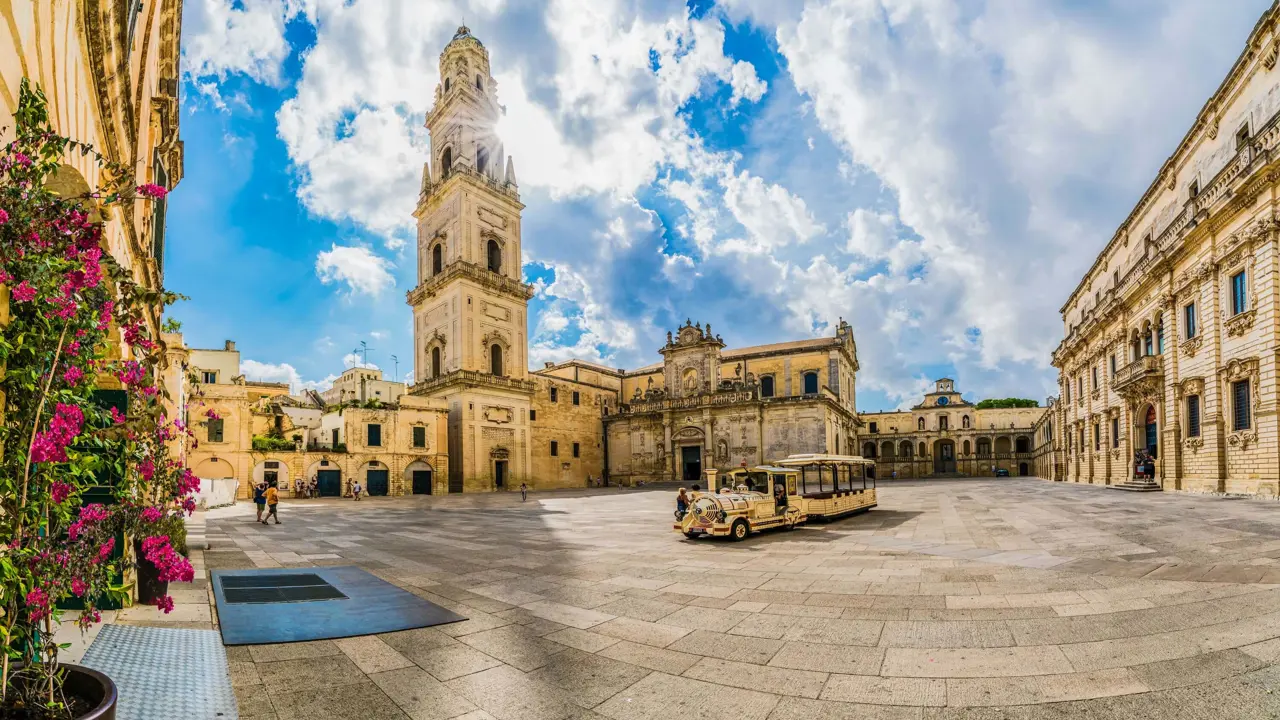 Square in Lecce, Italy, showing a tower and touring vehicle 