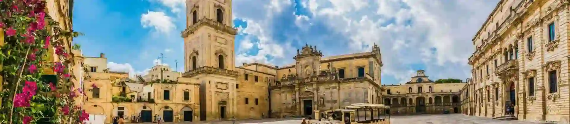 A square in Lecce, Puglia, Italy, featuring a historic tower and a land train for tourists