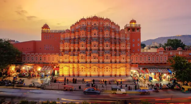 The Palace of the Winds in Jaipur illuminated at sunset, its ornate pink façade overlooking the street below