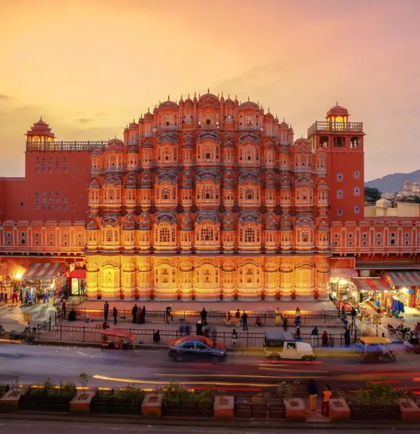 The Palace of the Winds in Jaipur illuminated at sunset, its ornate pink façade overlooking the street below