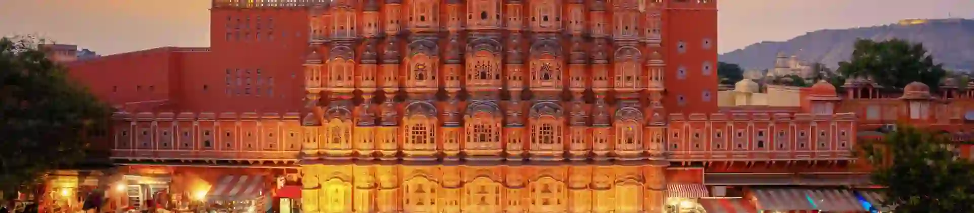 The Palace of the Winds in Jaipur illuminated at sunset, its ornate pink façade overlooking the street below