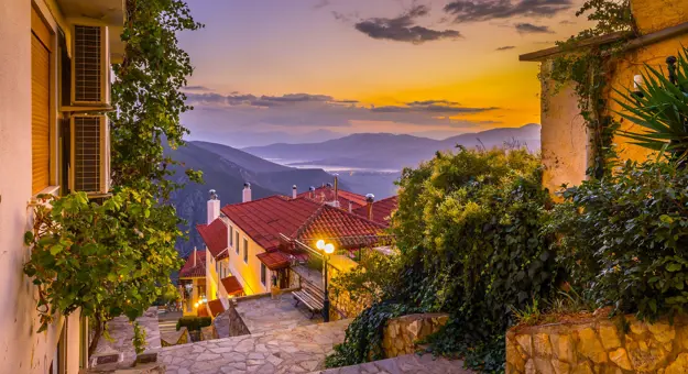 View from a village in the mountains, looking out on the landscape with sunset and silhouette of mountains. Steps and buildings in the forefront