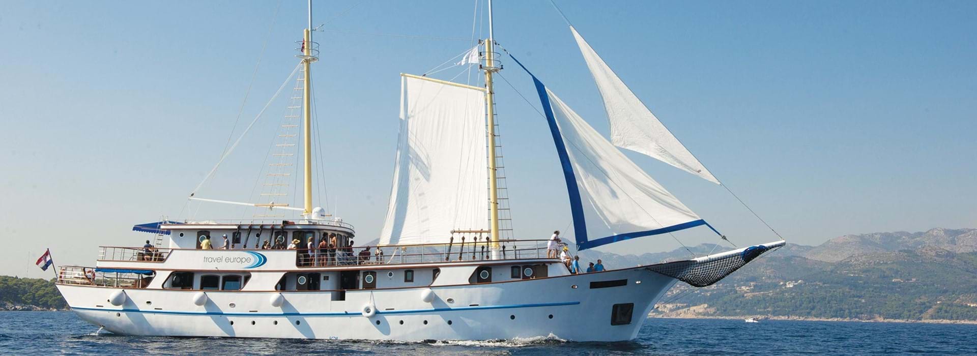 Shot of a sailing boat on water. With mountains to the right in the distance.