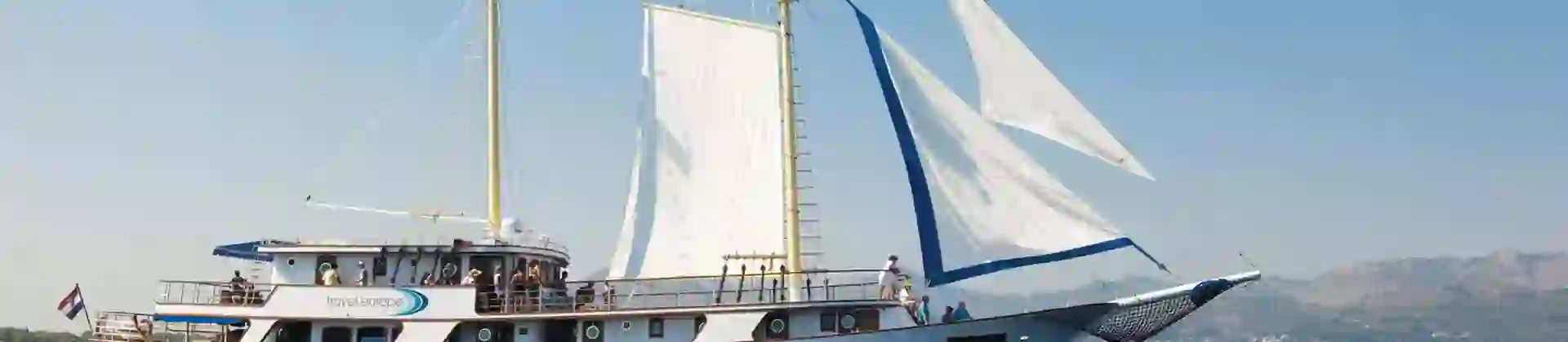 Shot of a sailing boat on water. With mountains to the right in the distance.