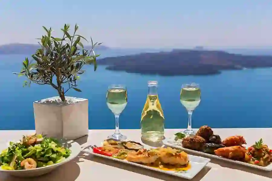 Three plates of Greek food, and 2 glasses and a bottle of wine, with view out to Greek Islands