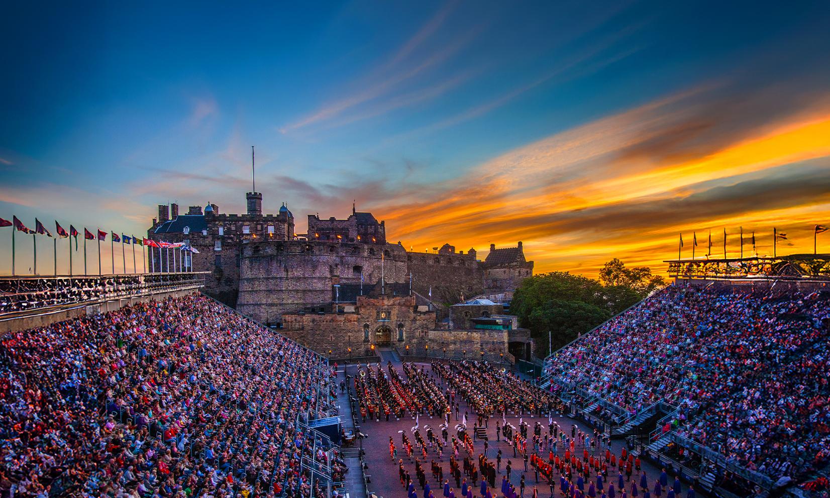 Edinburgh Castle at sunset overlooking a military parade during the The Royal Edinburgh Military Tattoo, with packed grandstands and rows of performers in uniform