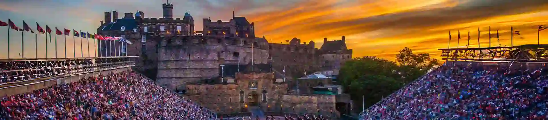 Edinburgh Castle at sunset overlooking a military parade during the The Royal Edinburgh Military Tattoo, with packed grandstands and rows of performers in uniform