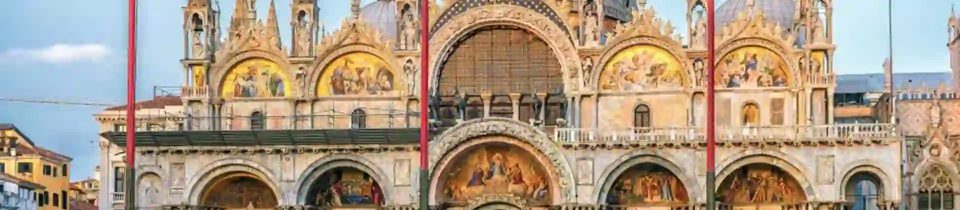 Exterior view of Saint Mark’s Basilica in Venice, Italy, showcasing its ornate façade with domes, arched windows, and detailed mosaics, reflecting Byzantine architectural style