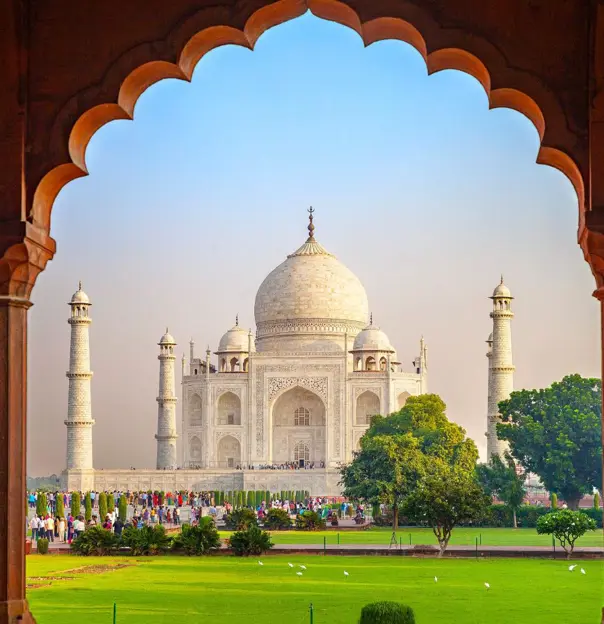 The Taj Mahal framed by an ornate archway, with green gardens in the foreground