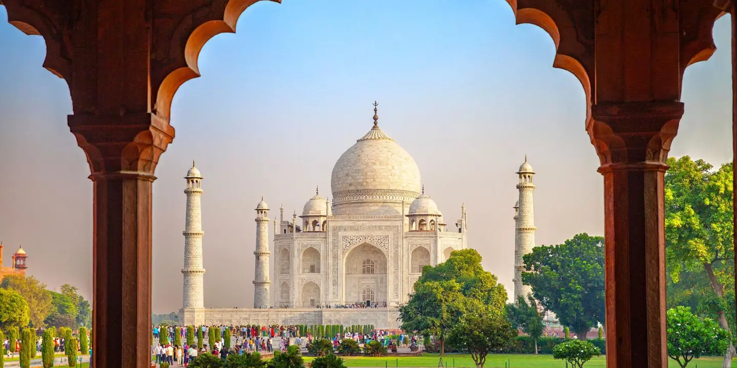 The Taj Mahal framed by an ornate archway, with green gardens in the foreground
