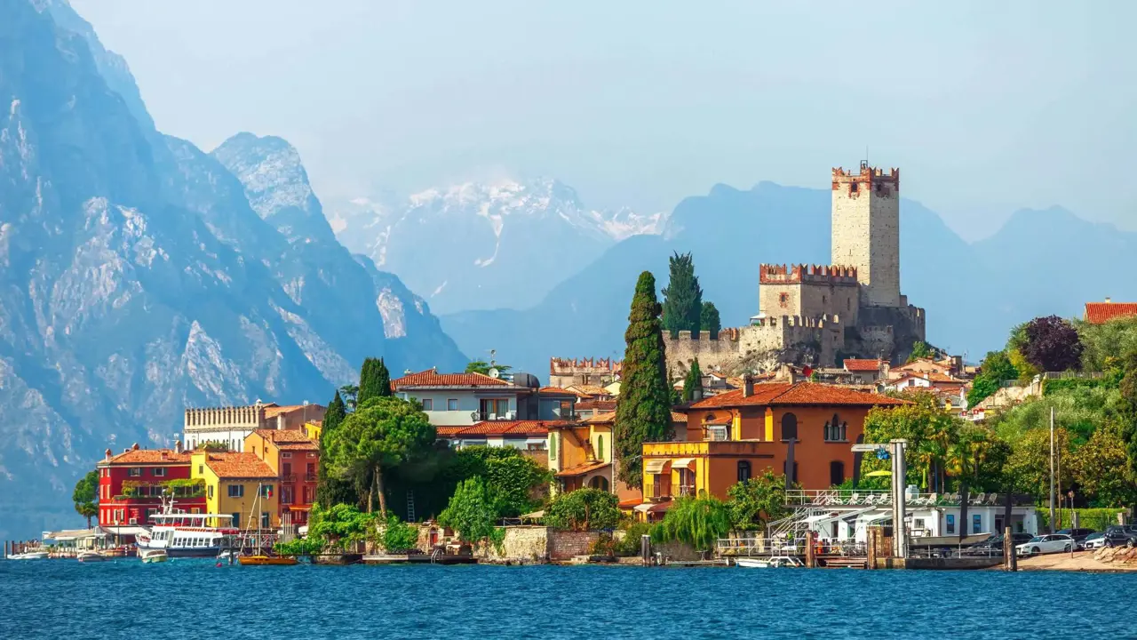 A scenic view of Malcesine on the shores of Lake Garda, Italy, with historic buildings, a medieval castle, and mountains in the background
