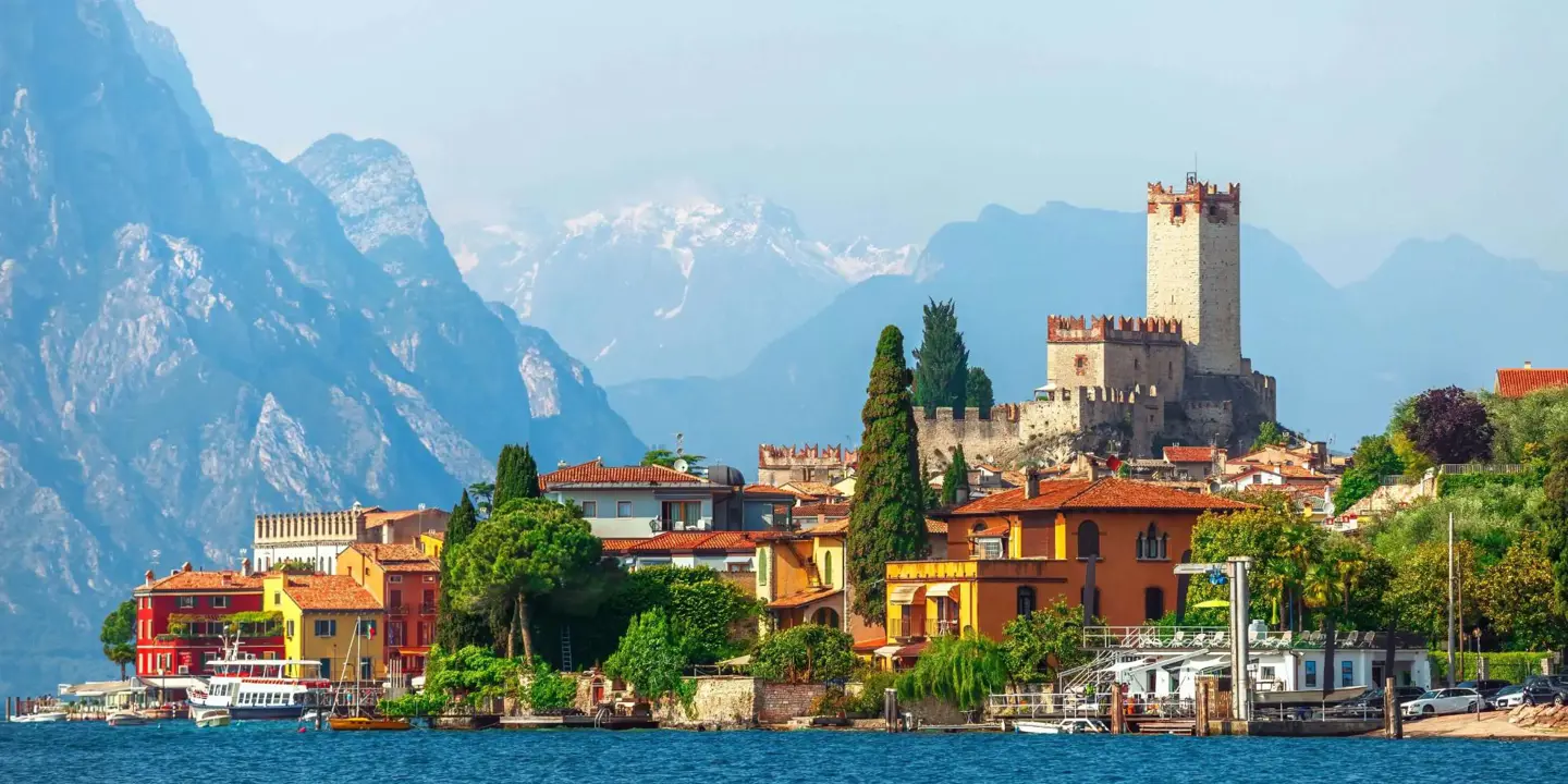 A scenic view of Malcesine on the shores of Lake Garda, Italy, with historic buildings, a medieval castle, and mountains in the background