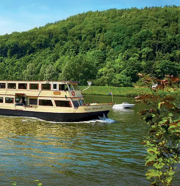 A private dinner cruise boat on the scenic Meuse River, surrounded by peaceful waters and lush green landscapes
