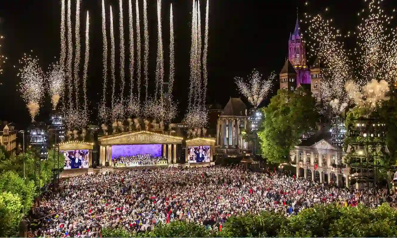André Rieu performing in Maastricht’s Vrijthof Square, with his orchestra on stage and colourful fireworks lighting up the night sky