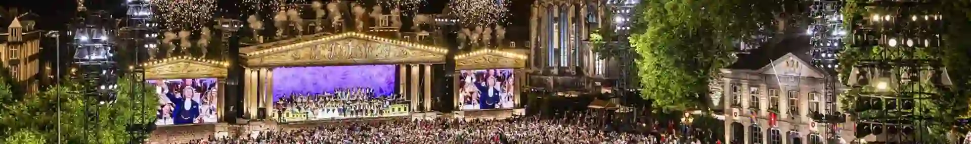 André Rieu performing in Maastricht’s Vrijthof Square, with his orchestra on stage and colourful fireworks lighting up the night sky