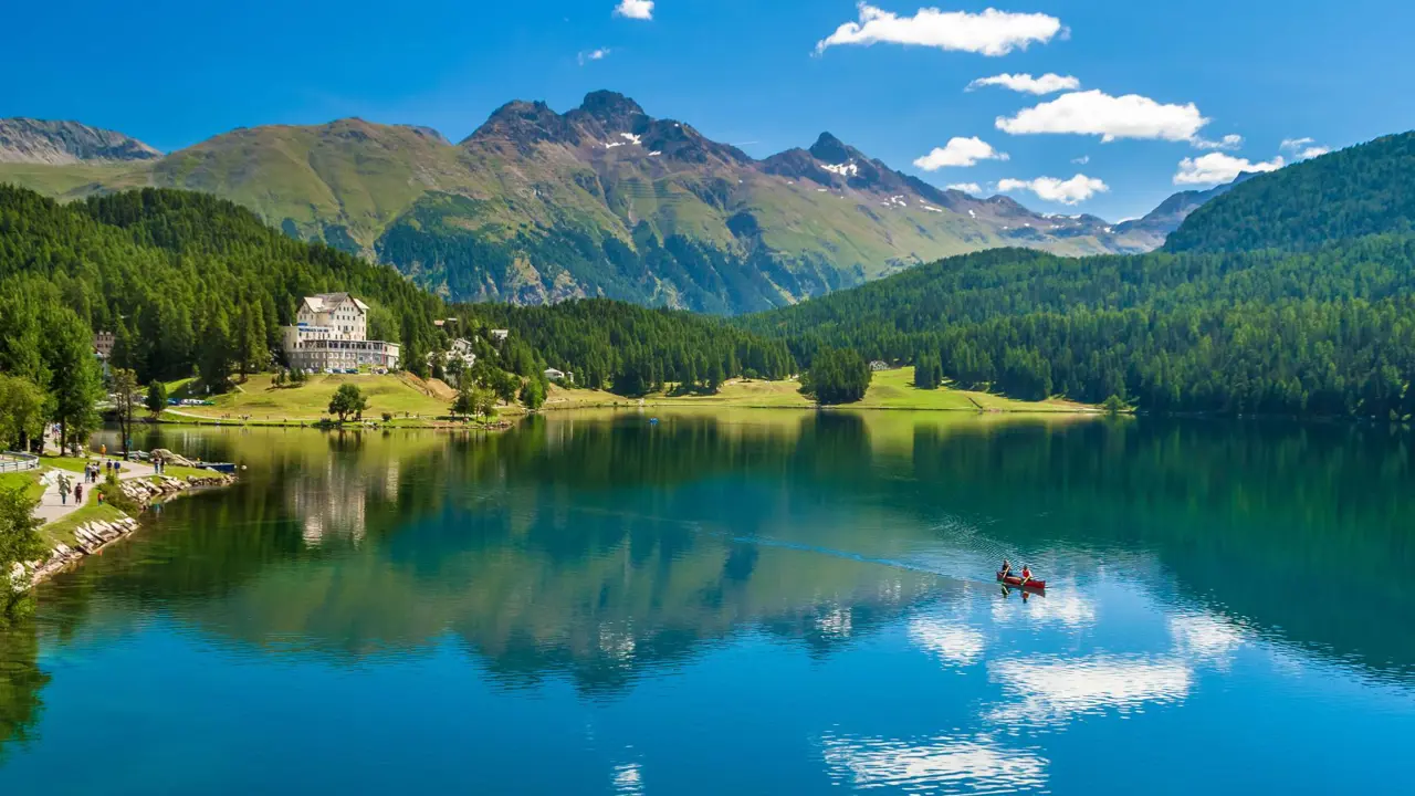 St Moritz Lake, Switzerland, showing a kayak travelling across the water, a large house on the bay and mountains in the background