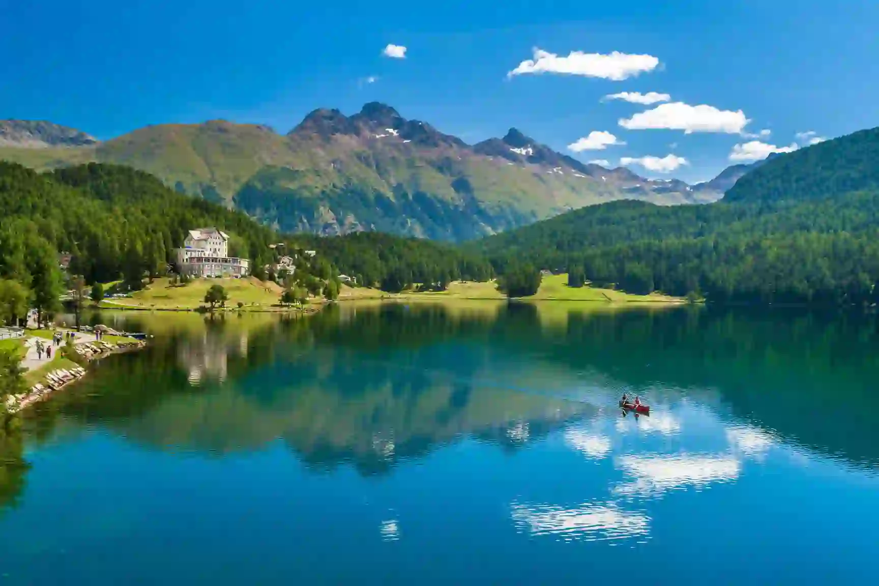 St Moritz Lake, Switzerland, showing a kayak travelling across the water, a large house on the bay and mountains in the background