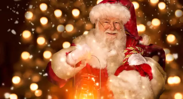 Santa holding a lantern and smiling, with a background of fairy lights