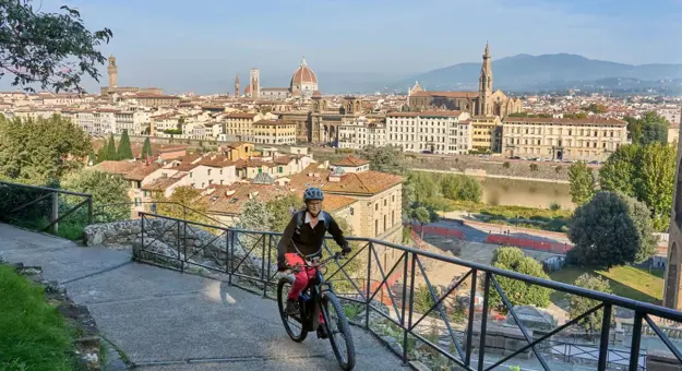 A woman cycling along a pathway on a mountain in Florence, with a view of the city in the background
