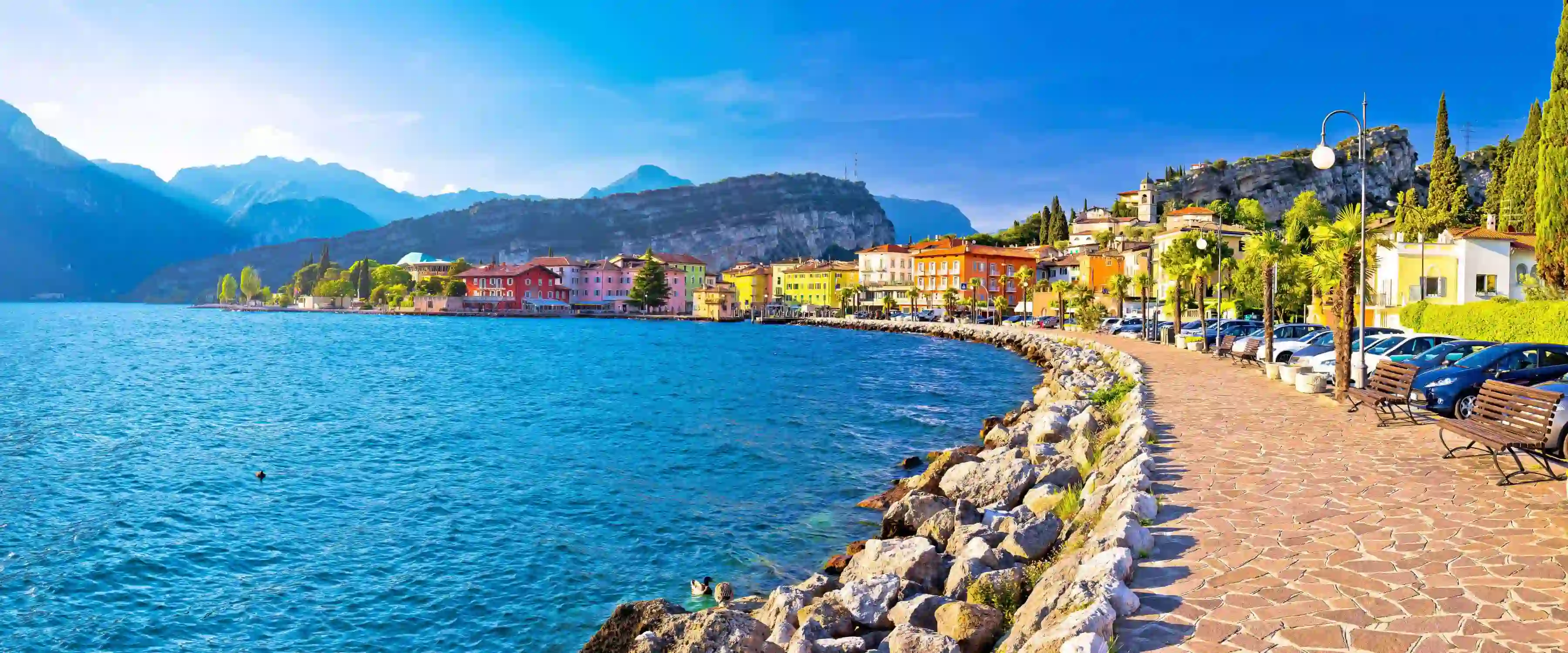 Waterfront in Torbole, Lake Garda, showing pavement and buildings and mountains in the distance