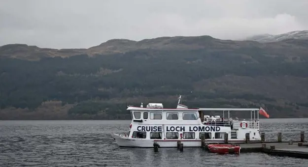 The 'Cruise Loch Lomond' boat moving along the water, with mountains behind it