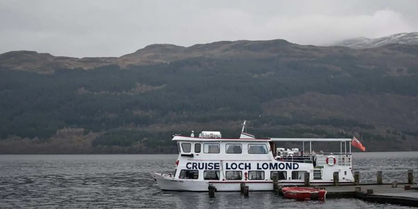 The 'Cruise Loch Lomond' boat moving along the water, with mountains behind it